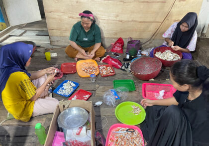 Warga pesisir Teluk Aru bekerja sama mengupas kepiting hasil tangkapan. Penelitian Universitas Pertamina menyoroti pentingnya diversifikasi pengolahan hasil laut sebagai jaring pengaman ekonomi saat musim paceklik melanda. (Foto: Dok. UPER)